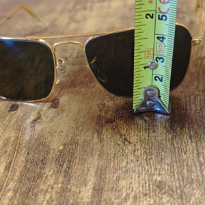 Puede incluir: Gafas de sol con montura dorada y lentes oscuras. Las gafas de sol se miden con una cinta m&eacute;trica. Las gafas de sol miden aproximadamente 5 cm de altura.