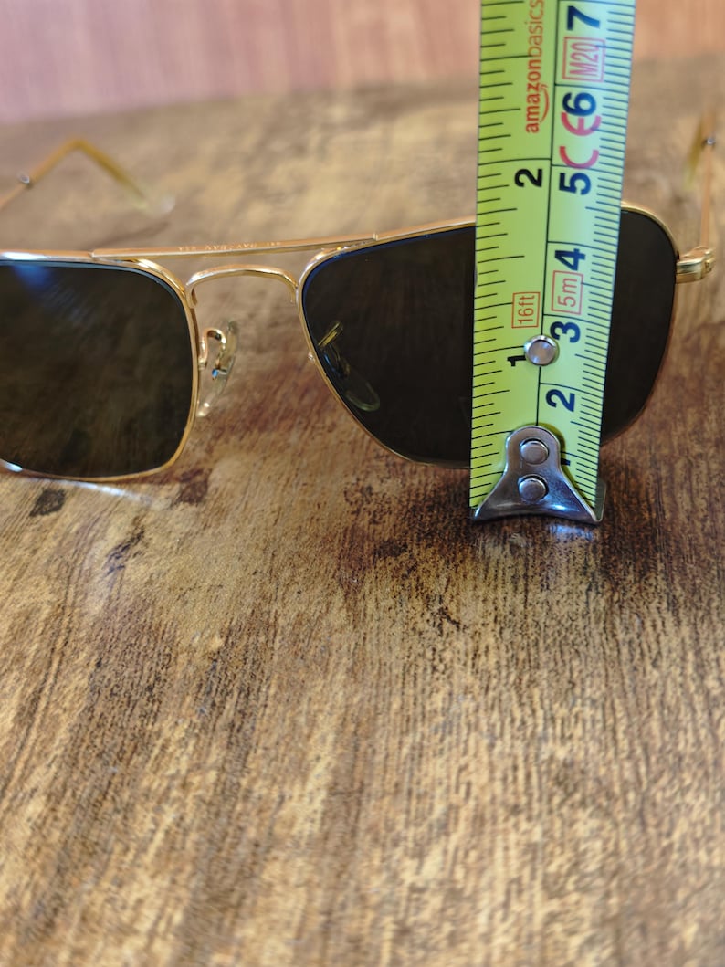 Puede incluir: Gafas de sol con montura dorada y lentes oscuras. Las gafas de sol se miden con una cinta m&eacute;trica. Las gafas de sol miden aproximadamente 5 cm de altura.