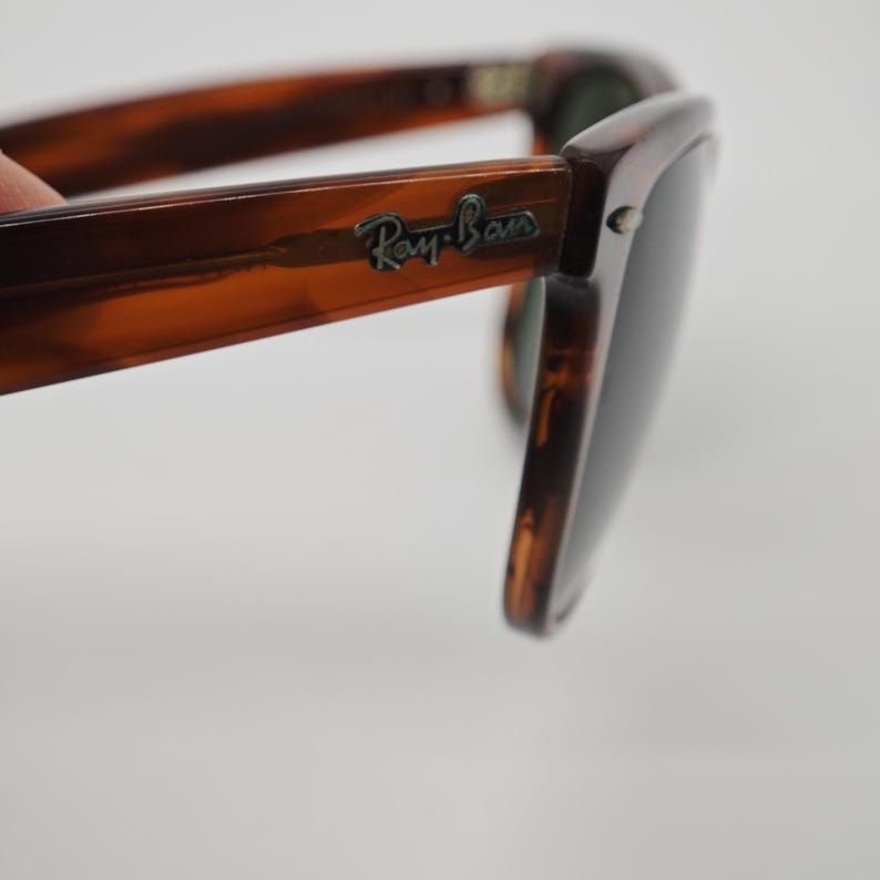 May include: Brown tortoiseshell sunglasses with dark lenses. The Ray-Ban logo is visible on the temple. The sunglasses have a classic, rectangular frame design.