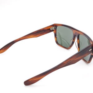 May include: Tortoiseshell sunglasses with rectangular frames and green lenses. The arms are a matching tortoiseshell pattern. The sunglasses are angled, showing the interior details of the frame and lenses.