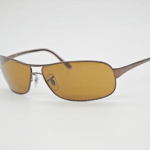 May include: Brown-framed sunglasses with amber-tinted lenses. The sunglasses have a sleek, modern design with a thin metal frame and a curved brow bar. The lenses are a warm, golden color, and the temples are slender and straight.