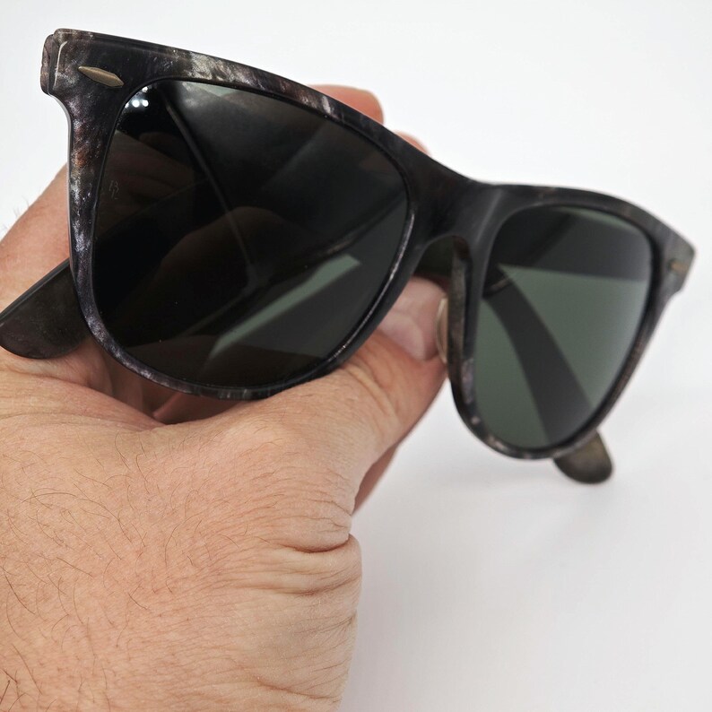 Puede incluir: Gafas de sol con un patr&oacute;n moteado negro y gris en las monturas. Las lentes son oscuras y las gafas de sol tienen una forma rectangular cl&aacute;sica. Las patillas tienen un patr&oacute;n moteado a juego.