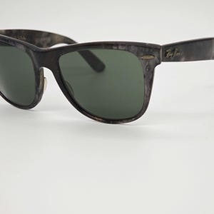 Puede incluir: Gafas de sol gris oscuro con lentes verdes. Las monturas tienen un patr&oacute;n veteado. El logotipo de Ray-Ban es visible en la patilla. Un accesorio de gafas cl&aacute;sico.