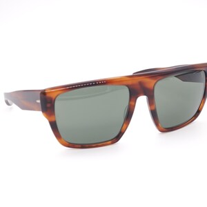May include: Tortoiseshell sunglasses with a rectangular frame and green lenses. The sunglasses have a classic design with a dark brown and amber pattern. The temples are a darker shade of brown.
