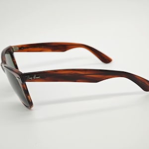 May include: Tortoiseshell sunglasses with dark lenses. The sunglasses have a classic Wayfarer style with a brown and black pattern. The Ray-Ban logo is visible on the left arm. The sunglasses are set against a white background.