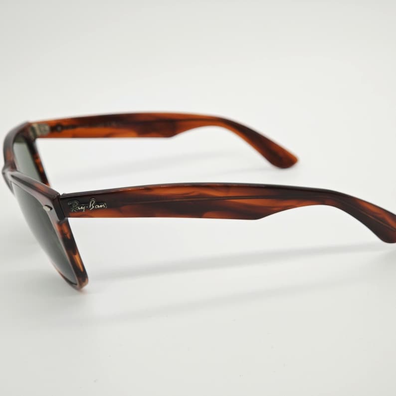 May include: Tortoiseshell sunglasses with dark lenses. The sunglasses have a classic Wayfarer style with a brown and black pattern. The Ray-Ban logo is visible on the left arm. The sunglasses are set against a white background.
