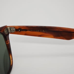 May include: Close-up of a pair of sunglasses with a brown tortoiseshell frame. The text "B&L RAY-BAN U.S.A." is visible on the arm of the sunglasses. The lenses are a dark green color.