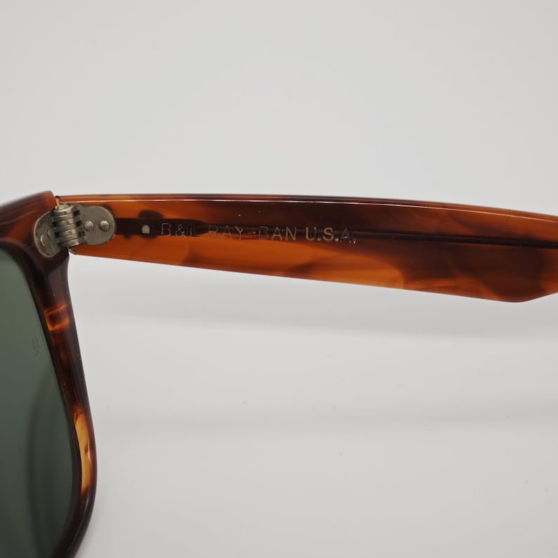 May include: Close-up of a pair of sunglasses with a brown tortoiseshell frame. The text "B&L RAY-BAN U.S.A." is visible on the arm of the sunglasses. The lenses are a dark green color.