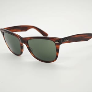 May include: Brown tortoiseshell sunglasses with green lenses. The sunglasses have a classic rectangular frame and a subtle logo on the temple. The glasses are set against a white background.