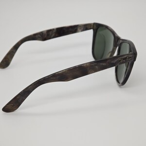 Puede incluir: Gafas de sol con un patr&oacute;n veteado marr&oacute;n y gris. Las lentes son de color verde oscuro. El logotipo de Ray-Ban es visible en la patilla. Las gafas de sol est&aacute;n sobre un fondo blanco.