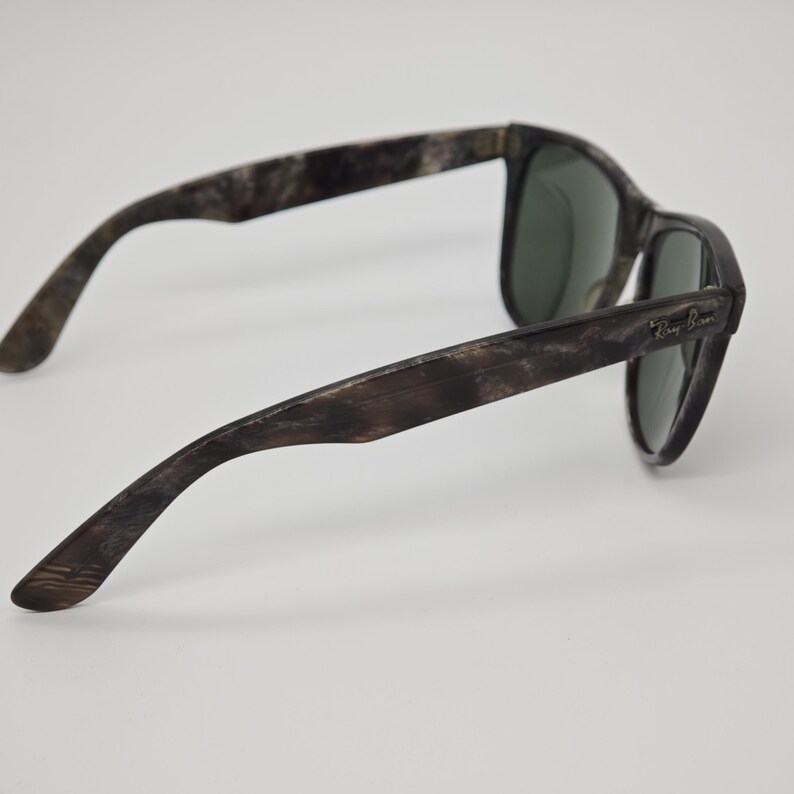 Puede incluir: Gafas de sol con un patr&oacute;n veteado marr&oacute;n y gris. Las lentes son de color verde oscuro. El logotipo de Ray-Ban es visible en la patilla. Las gafas de sol est&aacute;n sobre un fondo blanco.