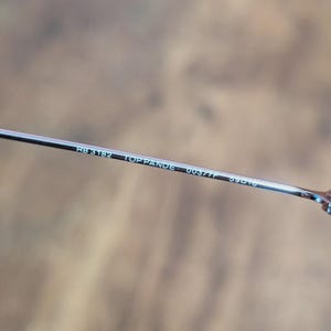 May include: Close-up of a silver metal eyeglass arm. The text "RB 3182 TOP PANDE 0037/F 59[]16" is printed in white on the arm. The background is a blurred, neutral tone.