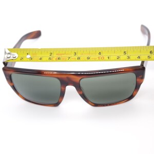 May include: Tortoiseshell sunglasses with dark lenses. The sunglasses measure approximately 5 inches across the frame. The frame has a classic, rectangular shape with a slightly curved top.
