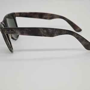 Puede incluir: Gafas de sol Ray-Ban con un patr&oacute;n veteado en gris oscuro y marr&oacute;n. Las gafas de sol tienen un estilo Wayfarer cl&aacute;sico con lentes oscuras y el logotipo de Ray-Ban en la patilla izquierda.