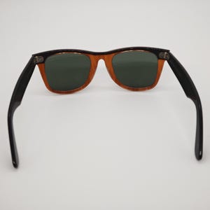 May include: Sunglasses with a classic design. The frames are a warm, translucent brown with black temples. The lenses are a dark green color, providing a contrast to the lighter frame. The sunglasses are set against a white background.
