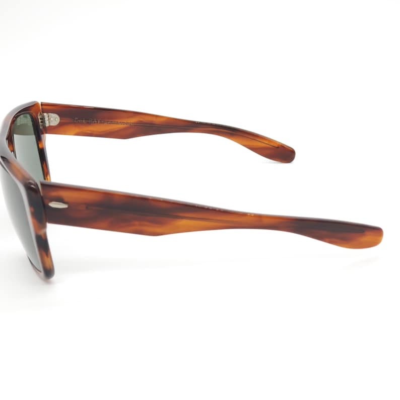 May include: Tortoiseshell sunglasses with dark lenses. The frames have a classic, rectangular shape with a subtle curve at the temples. The arms are a warm brown color, and the lenses are a dark green.