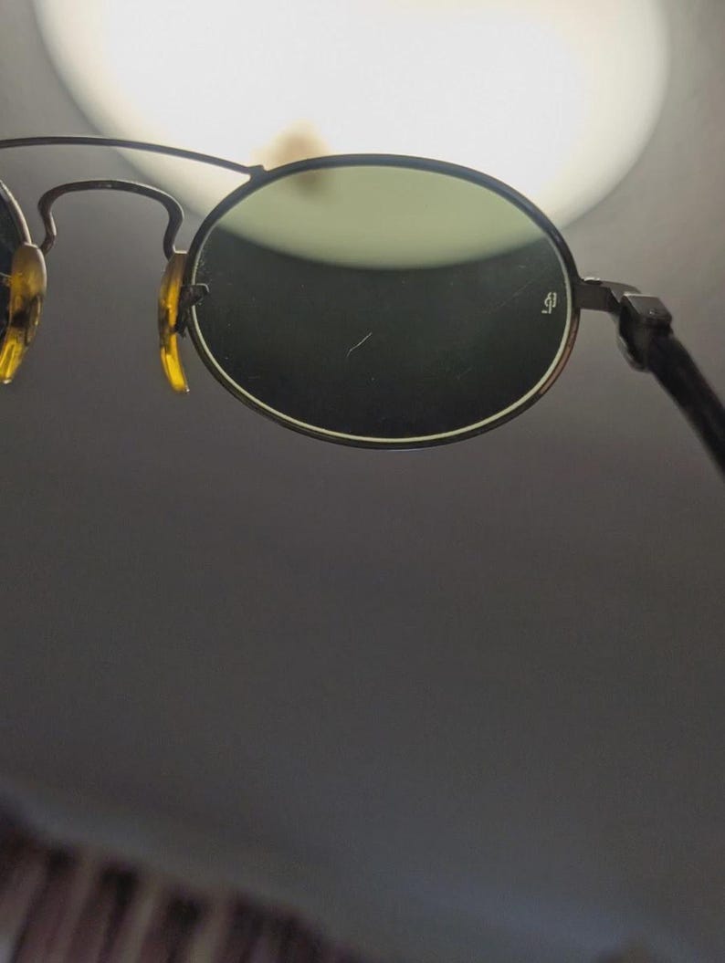 May include: Close-up of vintage sunglasses with round, green-tinted lenses. The frames are a dark metal with tortoise-shell accents on the temples. The lenses have a small logo on the right lens.