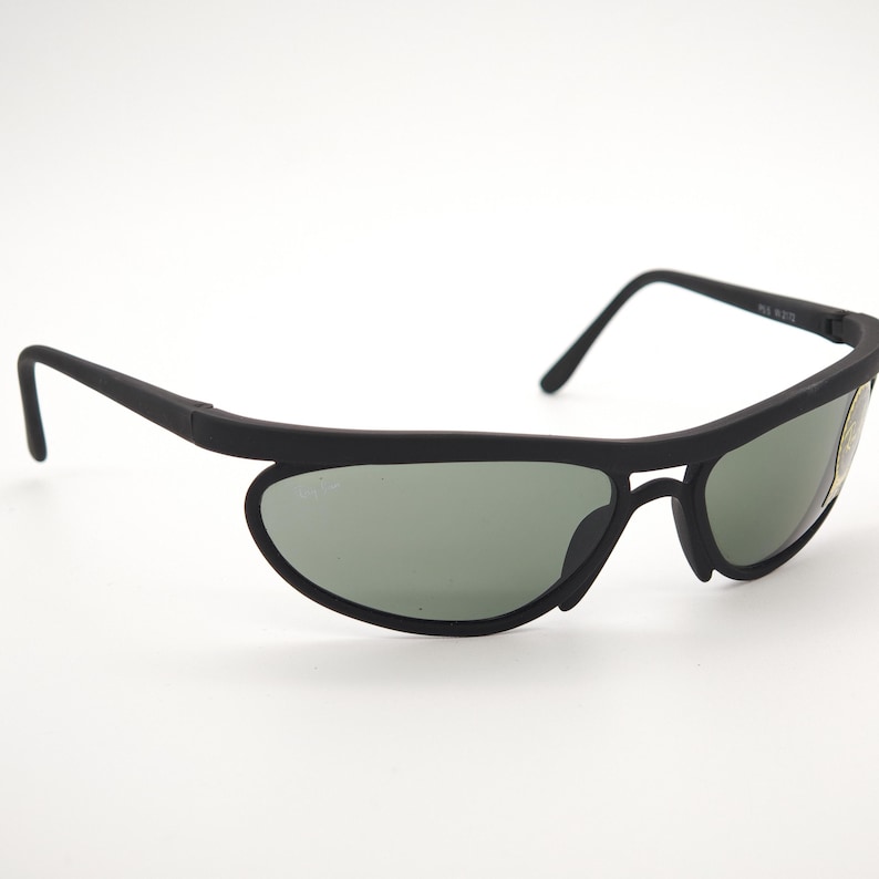 May include: Black sunglasses with a streamlined, curved design. The lenses are a muted green, set in a matte black frame. The arms curve down and back, giving a sporty and modern look.