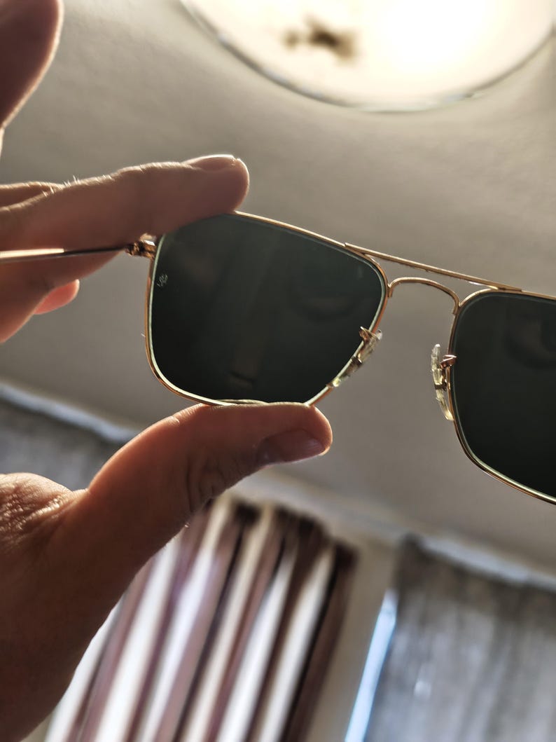 Puede incluir: Gafas de sol con montura dorada y lentes oscuras. Las gafas de sol tienen un dise&ntilde;o cl&aacute;sico de aviador con doble puente y lentes rectangulares. La montura es de color dorado brillante y las lentes son de color verde oscuro o negro.