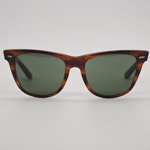 May include: Classic tortoiseshell sunglasses with green lenses. The frames have a brown and amber pattern. The sunglasses have a rectangular shape with a slightly curved top and a keyhole bridge.