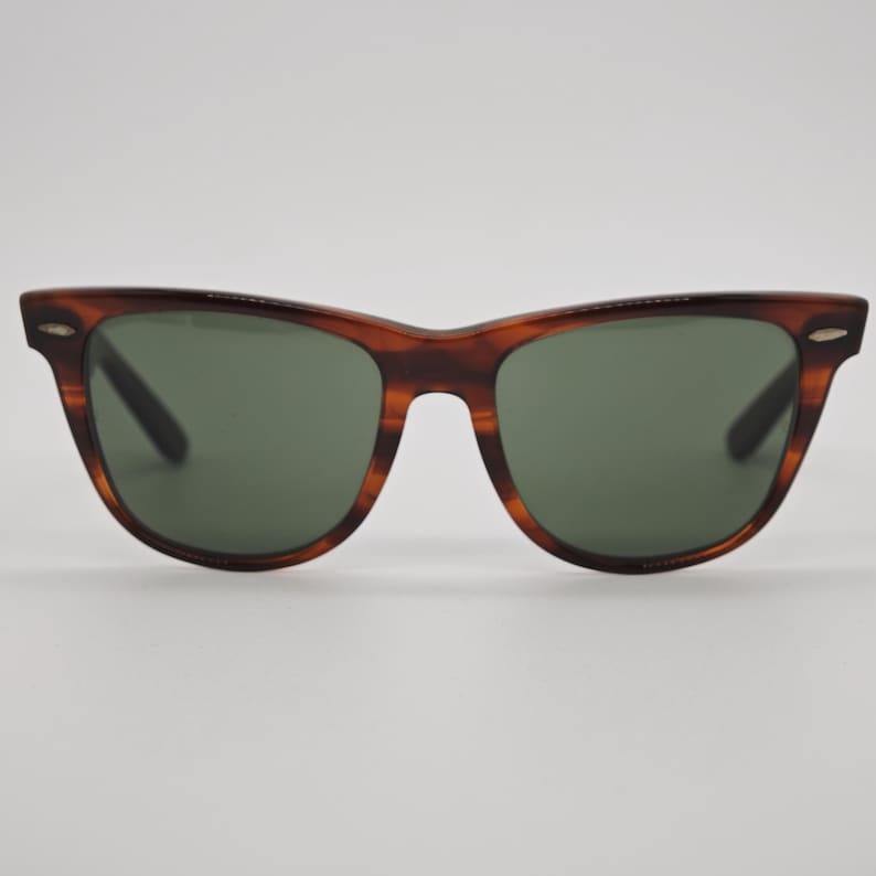 May include: Classic tortoiseshell sunglasses with green lenses. The frames have a brown and amber pattern. The sunglasses have a rectangular shape with a slightly curved top and a keyhole bridge.