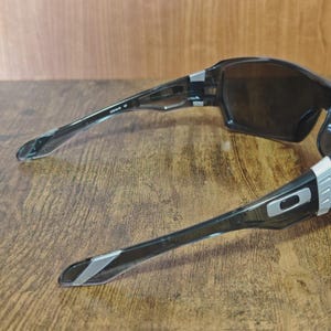 May include: Black sports sunglasses with dark lenses. The frames are black with silver accents on the temples and hinges. The sunglasses have a wraparound design.