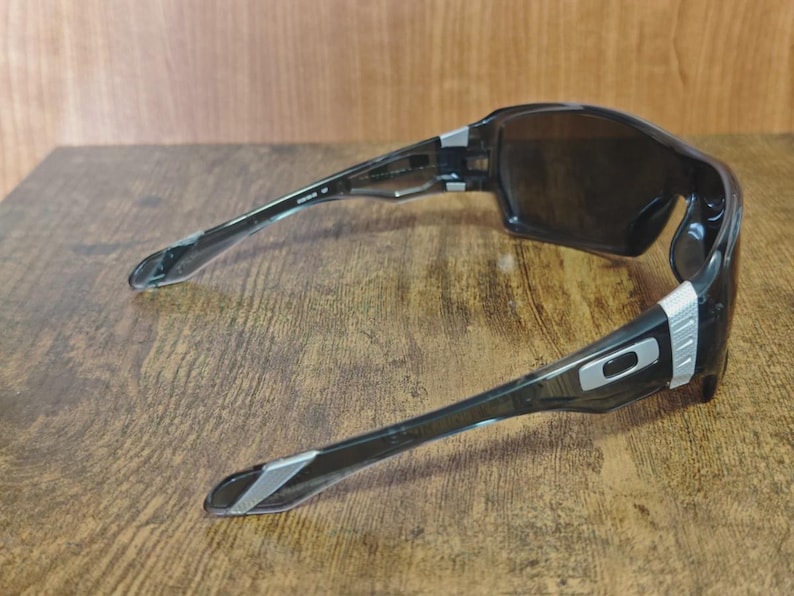 May include: Black sports sunglasses with dark lenses. The frames are black with silver accents on the temples and hinges. The sunglasses have a wraparound design.