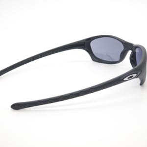 May include: Black sunglasses with gray lenses. The sunglasses have a sleek, curved design with textured arms and a small silver logo on the side. The lenses are a dark gray color, and the frame is matte black.