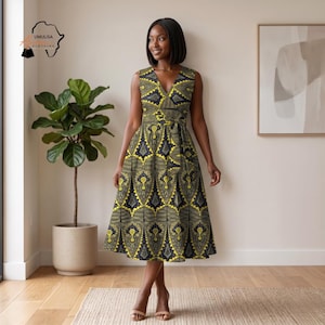 May include: A sleeveless, knee-length dress with a V-neck and a matching belt. The dress features a yellow and navy blue geometric pattern. The dress is worn by a person in a room with a plant and a framed picture.