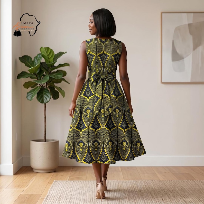 May include: A sleeveless, knee-length dress with a yellow and black geometric pattern. The dress features a bow at the waist and a flared skirt. The model is wearing nude heels. The dress is from Umulisa Clothing.