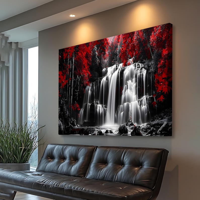 May include: A large canvas print of a waterfall scene. The image features a black and white waterfall cascading over rocks, surrounded by red trees and foliage. The artwork is displayed on a gray wall above a black leather sofa.