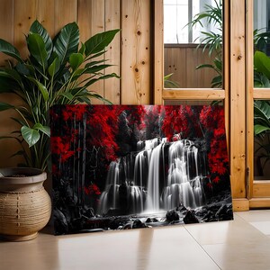 May include: A canvas print depicting a waterfall scene with a striking contrast of black, white, and red. The cascading water is rendered in shades of white, set against a backdrop of black trees and vibrant red foliage. The artwork is displayed indoors.