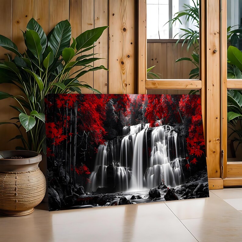 May include: A canvas print depicting a waterfall scene with a striking contrast of black, white, and red. The cascading water is rendered in shades of white, set against a backdrop of black trees and vibrant red foliage. The artwork is displayed indoors.