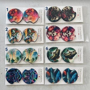 Puede incluir: Ocho juegos de dos posavasos circulares para coche en envases de plástico transparente, numerados del uno al ocho. Los diseños incluyen patrones florales, calaveras con rosas, paisajes, un pez, setas y un banco de peces, todos etiquetados.