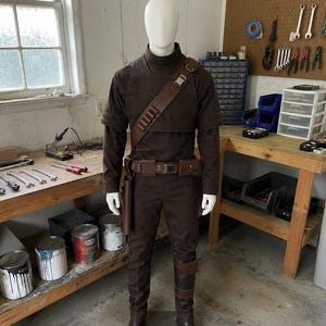 Din Djarin Mandalorian cosplay costume inspired by The Mandalorian featuring tactical vest, matching belt, fitted shirt, and tailored pants. Beskar inspired bounty hunter outfit designed for cosplay events, conventions, Halloween, roleplay, and collectors. Handmade Star Wars inspired costume with cinematic styling, premium craftsmanship, and comfortable convention-ready fit.
