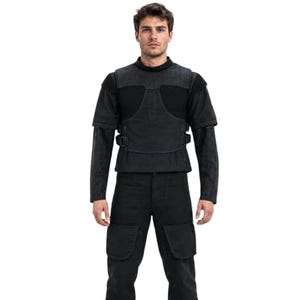 May include: Black tactical outfit featuring a short-sleeved vest with buckle closures over a long-sleeved shirt. The outfit includes matching black cargo pants with large pockets. The model is wearing black boots.