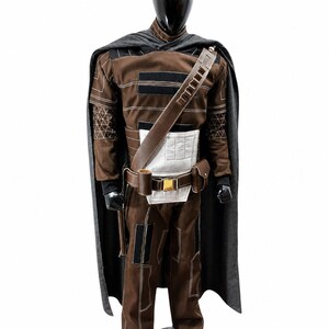 May include: A brown and black costume displayed on a mannequin. The costume includes a long-sleeved top, pants, belt, and shoulder strap. A gray cape is draped over the shoulders. The costume has white and black accents and a gold buckle.