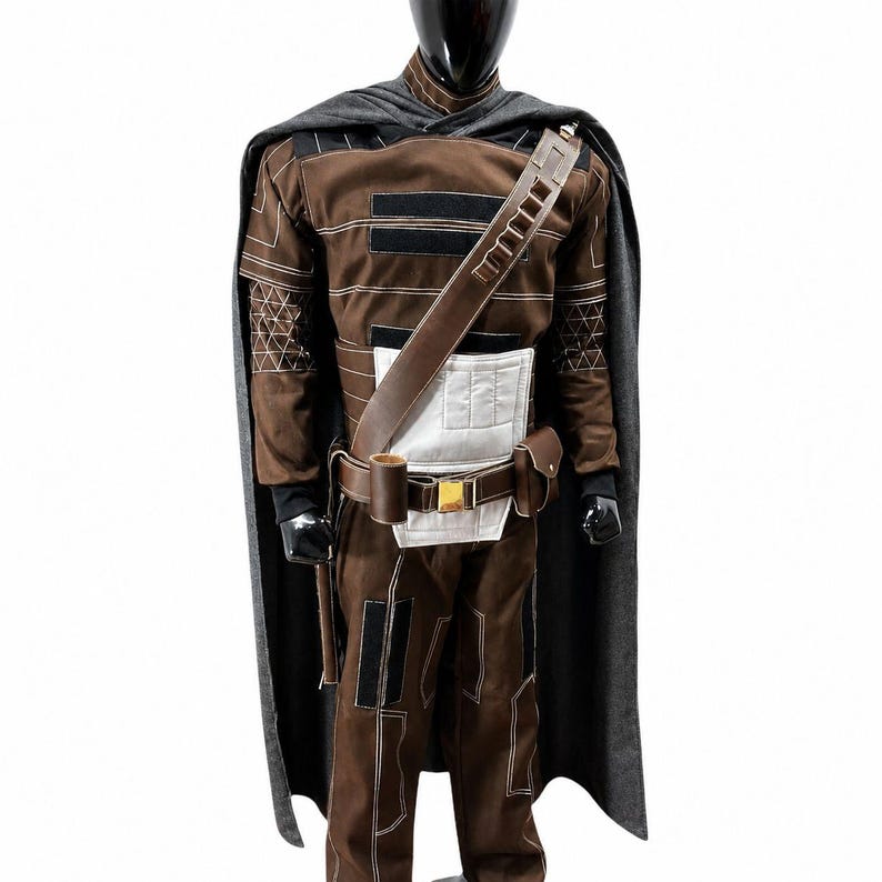 May include: A brown and black costume displayed on a mannequin. The costume includes a long-sleeved top, pants, belt, and shoulder strap. A gray cape is draped over the shoulders. The costume has white and black accents and a gold buckle.