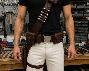 May include: A brown leather utility harness featuring a cross-body strap with a small pouch and five silver-toned cylindrical accents. The waist belt includes two side pouches, a central silver buckle, and a drop-leg holster with a thigh strap.