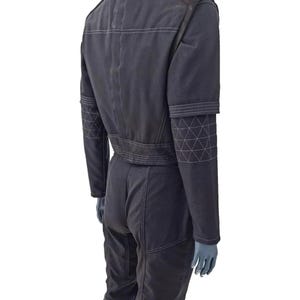 K&ouml;nnte beinhalten: Dunkelgrauer Overall mit wei&szlig;en Steppn&auml;hten. Der Overall hat einen G&uuml;rtel in der Taille, lange &Auml;rmel und geometrische Muster an den Oberarmen. Das Kleidungsst&uuml;ck wird auf einer Schaufensterpuppe pr&auml;sentiert.