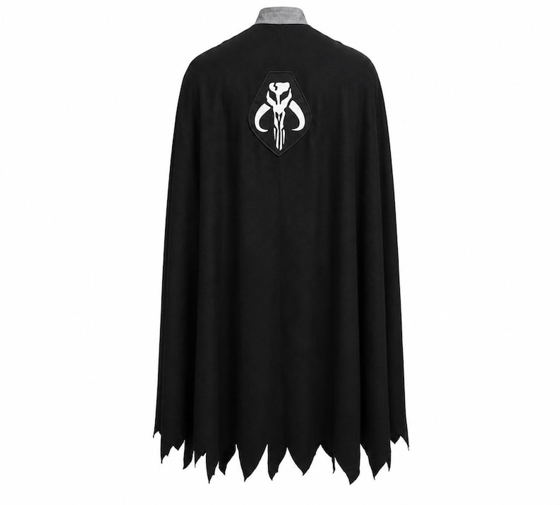 May include: A black cape featuring a grey collar and a white Mythosaur skull emblem centered on the upper back. The hem of the cape is cut into a jagged, pointed design, creating a distinct silhouette. The fabric appears solid and opaque.