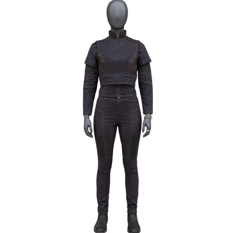 May include: A dark gray two-piece outfit displayed on a mannequin. The outfit includes a long-sleeved, cropped jacket with a high collar and matching pants. The jacket has a layered design, and the pants are fitted. The outfit is made of a textured fabric.