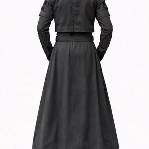 May include: A dark gray outfit featuring a cropped jacket with structured shoulders and long sleeves, paired with a long, flowing skirt. The outfit is cinched at the waist with a matching belt, and the model is wearing dark pants and shoes.