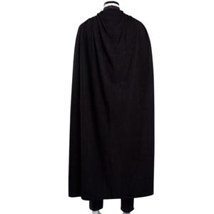 May include: A long, black cape with a draped hood. The cape is made of a dark, possibly wool-like material, and falls to the ankles. The image is a rear view, showing the full length of the garment.