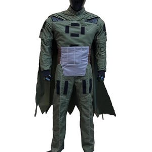 May include: A green military-style costume with a cape. The outfit includes a jacket, pants, and a cape, all in a similar shade of green. The jacket has black patches and a gray belt. The costume is designed to resemble a military uniform.