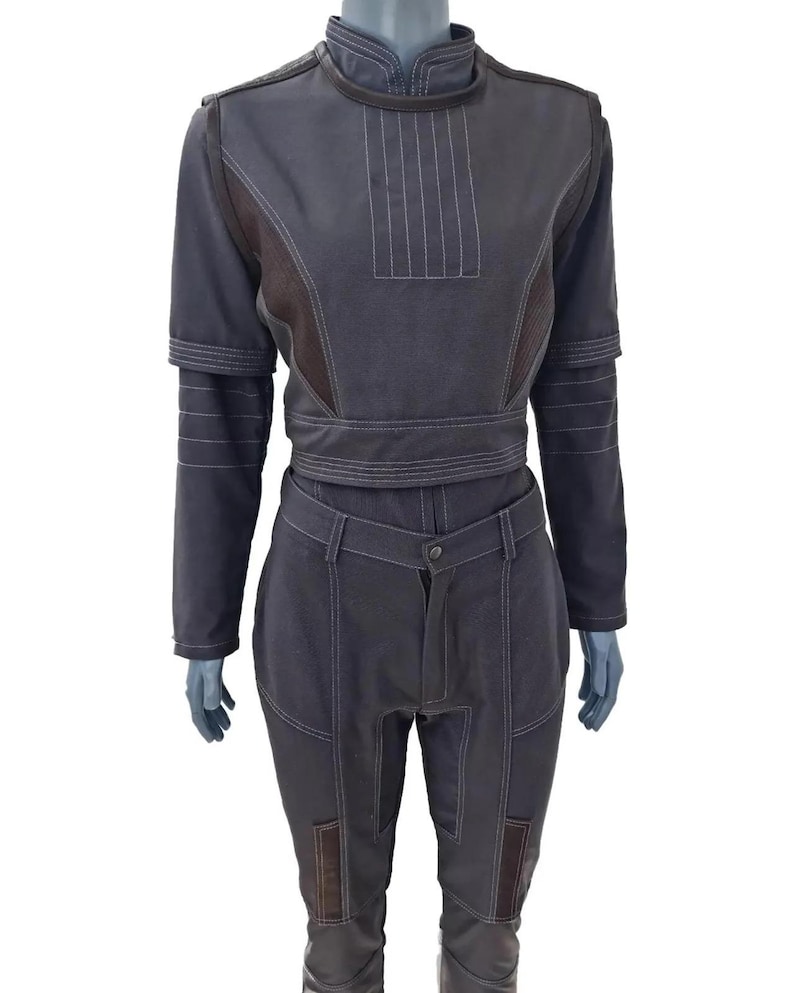 K&ouml;nnte beinhalten: Ein dunkelgraues zweiteiliges Outfit mit wei&szlig;en N&auml;hten. Das Oberteil hat einen hohen Kragen und lange &Auml;rmel. Die Hose hat einen Knopfverschluss und Taschen. Das Outfit wird auf einer Schaufensterpuppe pr&auml;sentiert.