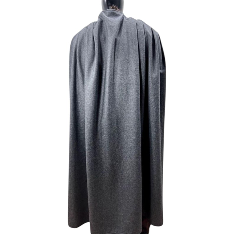 Może przedstawiać: Szary płaszcz wykonany z miękkiej, teksturowanej tkaniny. Peleryna jest długa, sięga do kostek i opada na ramiona. Widok z tyłu pokazuje całą długość peleryny i spos&oacute;b jej opadania.