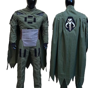 May include: A green costume with a cape, displayed on a mannequin. The costume features a chest plate, a utility belt, and a cape with a black and white emblem on the back. The outfit is designed with multiple pockets and black accents.