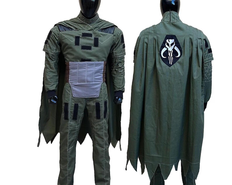 May include: A green costume with a cape, displayed on a mannequin. The costume features a chest plate, a utility belt, and a cape with a black and white emblem on the back. The outfit is designed with multiple pockets and black accents.