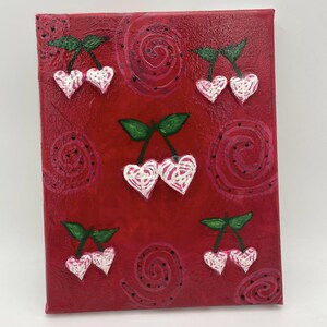 May include: A red canvas art piece featuring white heart-shaped cherries with green leaves. The background has a textured appearance with painted swirls and dots. The artwork is a unique decorative piece.